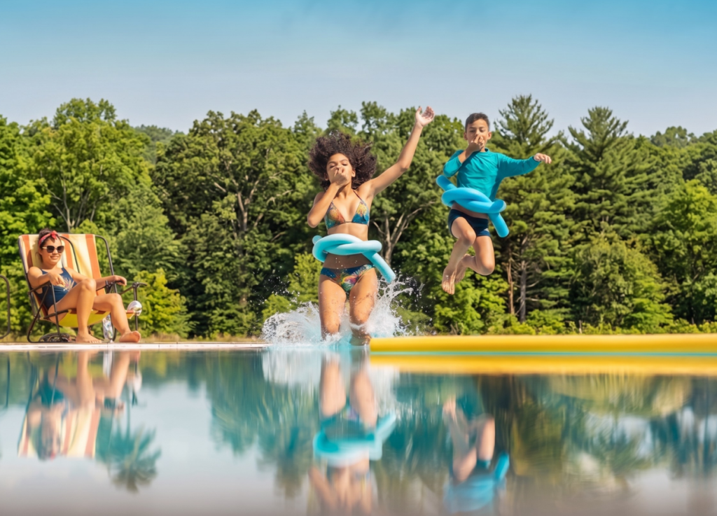 Two young people jumping into a pool, as an adult watches, ensuring pool party safety.